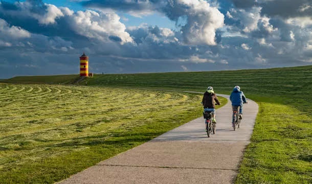 Zwei Radfahrer genießen die Landschaft in Greetsiel, mit dem markanten Leuchtturm im Hintergrund.